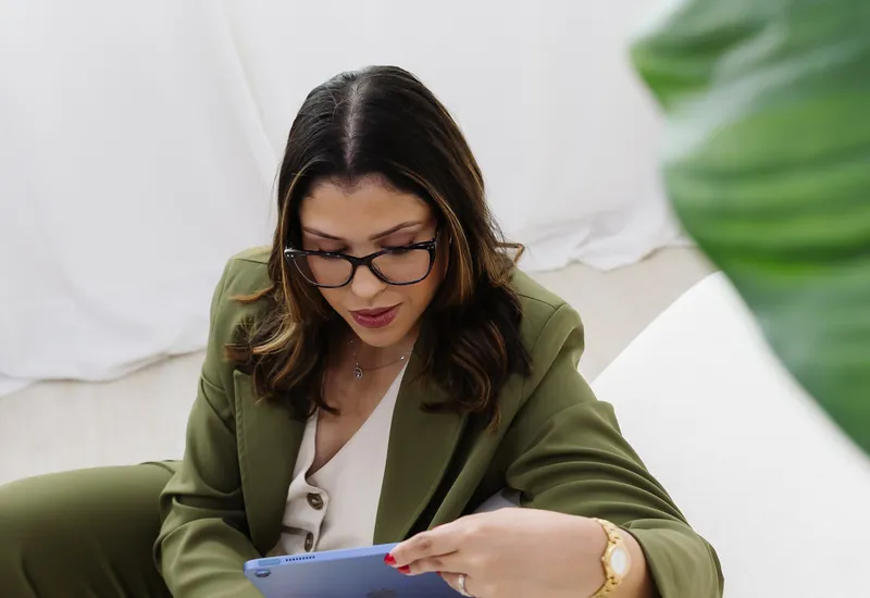 Emanuelle Mendes de óculos, sentada, olhando para o tablet